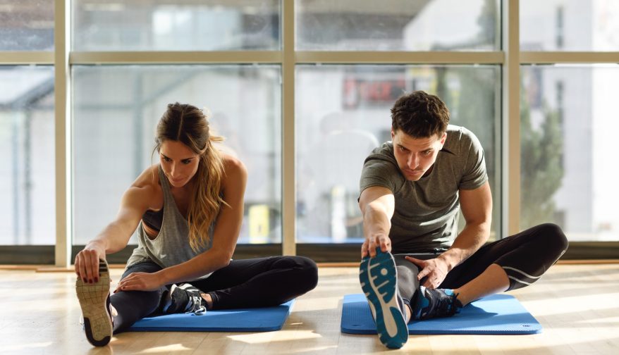 Young woman and man working out indoors. Two people streching their legs on the floor of a gym.